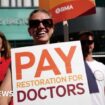 Photo of a striking doctor in glasses holding a placard, which reads 'pay restoration for doctors'