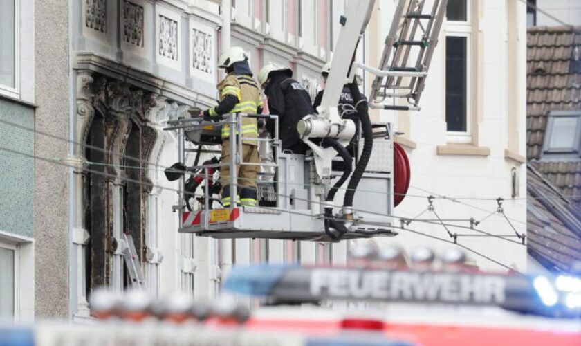 Solingen: Feuerwehrmänner stehen vor einem Mehrfamilienhaus, in dem es gebrannt hat, im Korb einer Drehleiter