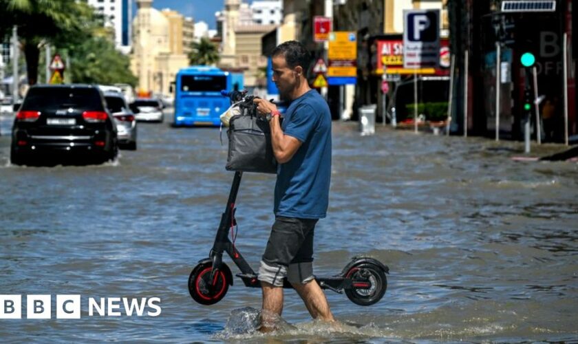 Man carrying a scooter with water up to his knees in Dubai