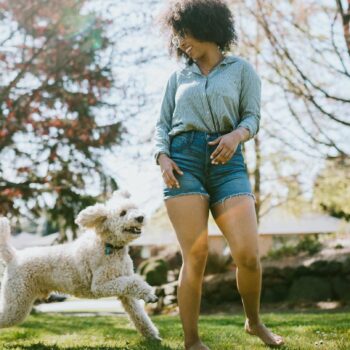 Eine Frau in kurzen Hosen spielt mit einem Hund auf der Wiese