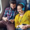 Junges Paar sitzt im Zug und surft im Internet