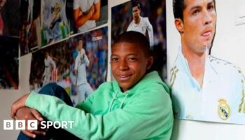 Kylian Mbappe sits on his bed with posters of Real Madrid's Cristiano Ronaldo all around him