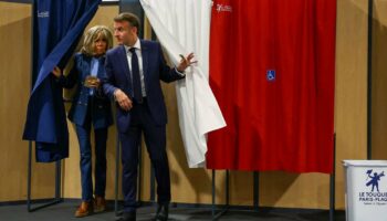 Le président français Emmanuel Macron (à droite) et son épouse Brigitte Macron (à gauche) sortent d'un isoloir, orné de rideaux arborant les couleurs du drapeau français, avant de voter pour l'élection du Parlement européen dans un bureau de vote au Touquet, dans le nord de la France, le 9 juin 2024.
