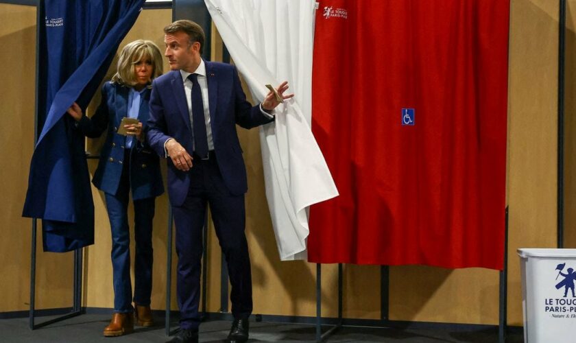 Le président français Emmanuel Macron (à droite) et son épouse Brigitte Macron (à gauche) sortent d'un isoloir, orné de rideaux arborant les couleurs du drapeau français, avant de voter pour l'élection du Parlement européen dans un bureau de vote au Touquet, dans le nord de la France, le 9 juin 2024.