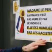 Un manifestant colle une affiche clamant "Madame Le Pen, la France n'est pas humiliée par les noirs, elle est humiliée par les racistes" sur le siège du Rassemblement national lors d'une manifestation de SOS Racisme en soutien à la chanteuse Aya Nakamura, à Paris, le 24 mars 2024