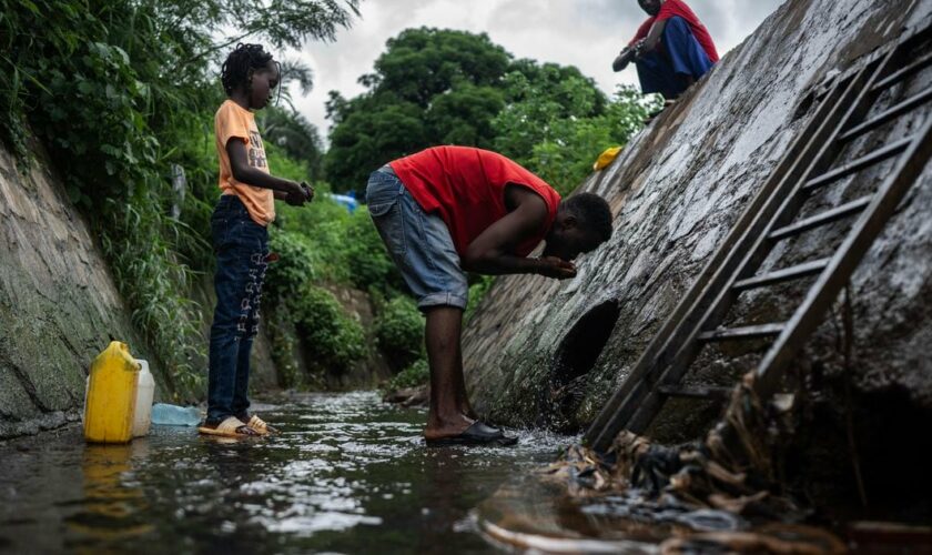 A man drinks water from a wastewater stream in a makeshift camp where migrants live at the Cavani stadium in Mamoudzou on the French island of Mayotte, on February 15, 2024. France's Minister of the Interior Gerald Darmanin announced on February 11, 2024, a constitutional amendment to eliminate "Jus Soli", the acquisition of citizenship by birth within a territory, on the Indian Ocean island of Mayotte, which faces an ongoing migration crisis. (Photo by JULIEN DE ROSA / AFP)