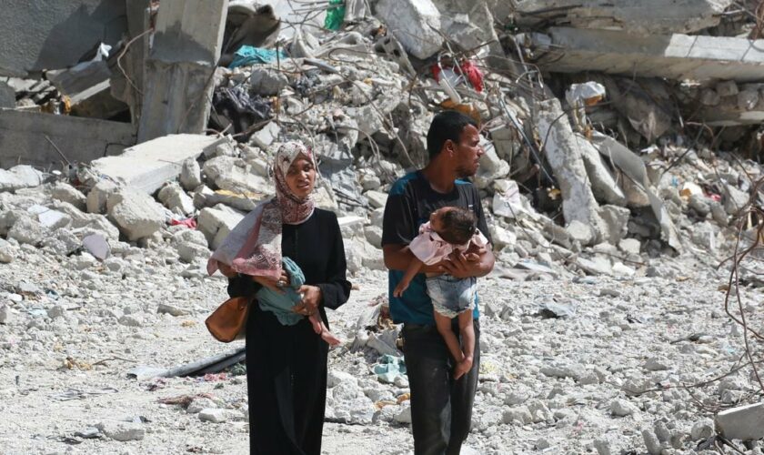 Un couple palestinien tenant ses enfants dans les bras marche au milieu des destructions à Khan Younès, dans le sud de la bande de Gaza, le 4 juillet 2024