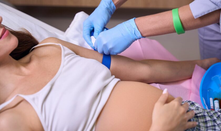 Cropped image of female nurse preparing hand of young pregnant woman to injection on medical bed in hospital. Concept of pregnancy and maternity