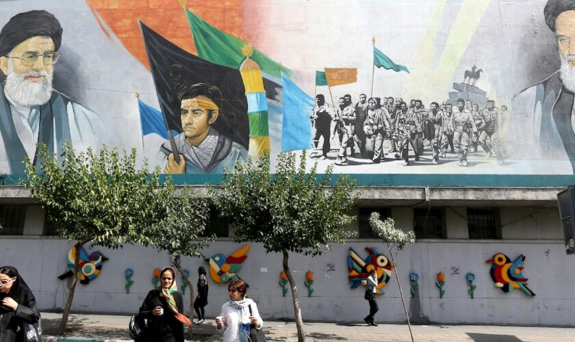 Des Iraniennes marchent dans une rue de Téhéran devant une fresque murale où figurent le guide suprême iranien Ali Khamenei (G), et le fondateur de la République islamique d'Iran, l'ayatollah Khomeiny (D), le 6 juillet 2024 au lendemain de l'élection présidentielle