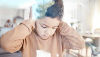 Sad, home and boy with hands on ears for depression, fear and scared of conflict with family by window. Child psychology, autism and depressed, anxiety and upset kid in living room for mental health