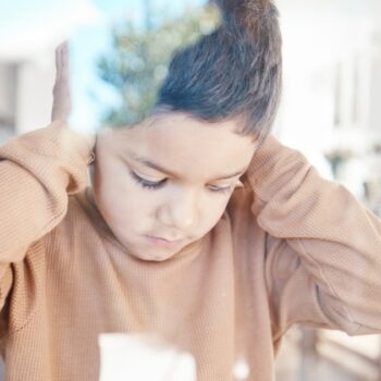 Sad, home and boy with hands on ears for depression, fear and scared of conflict with family by window. Child psychology, autism and depressed, anxiety and upset kid in living room for mental health