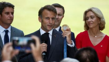 Le président de la République Emmanuel Macron, au centre, tient une médaille d'or des Jeux de Paris 2024, le 12 août 2024, à Paris