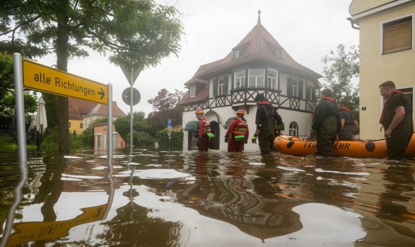 Feuerwehrleute und Wasserretter waten durch eine überflutete Straße.