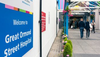 London, UK - A welcome sign outside the NHS Great Ormond Street Hospital for Children in London, with people by the entrance in the background.