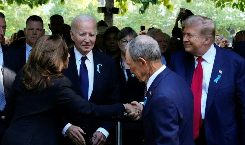 La vice-présidente américaine et candidate démocrate Kamala Harris (de dos) serre la main de l'ancien président républicain Donald Trump, sous les regards du président sortant Joe Biden (de face) et de l'ancien maire de New York Michael Bloomberg (de dos) à la cérémonie du 23e anniversaire des attentats du 11-Septembre 2001, à Manhattan le 11 septembre 2021.