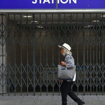 Une passante marche devant les grilles fermées de la station de métro Victoria à Londres le 19 août 2022, alors que le réseau de transports en commun de la capitale britannique est très perturbé par une grève pour les salaires face à l'inflation