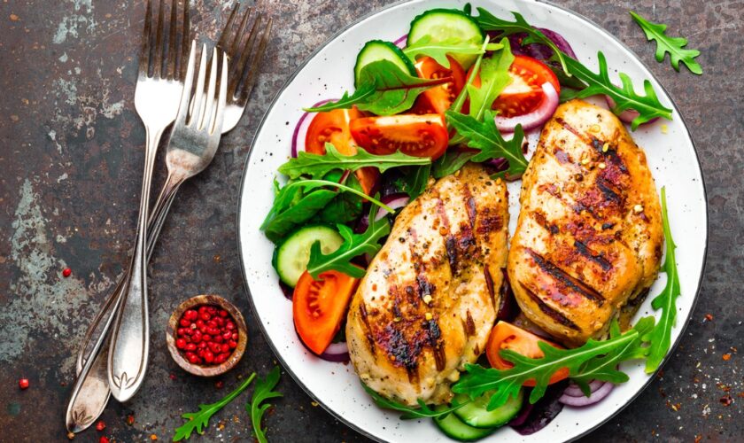 Grilled chicken breast. Fried chicken fillet and fresh vegetable salad of tomatoes, cucumbers and arugula leaves. Chicken meat with salad. Healthy food. Flat lay. Top view. Dark background