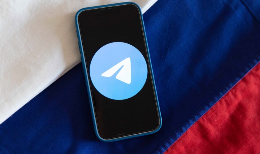 Illustration montrant le logo de l'application de messagerie Telegram affiché sur un téléphone portable avec les couleurs du drapeau russe