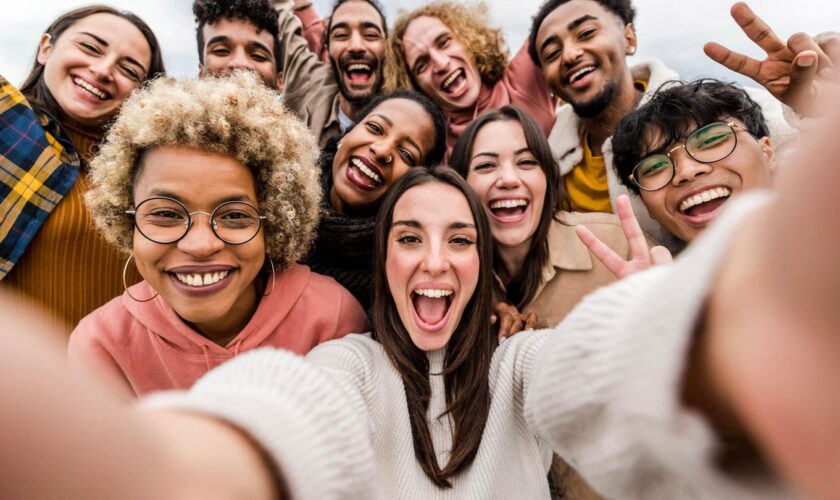 Eine Frau lacht mit vielen Freundin auf einem Selfie.